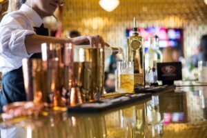 Bartender pouring a craft cocktail over ice at a stylish Treasure Island bar, with copper barware and warm ambient lighting.
