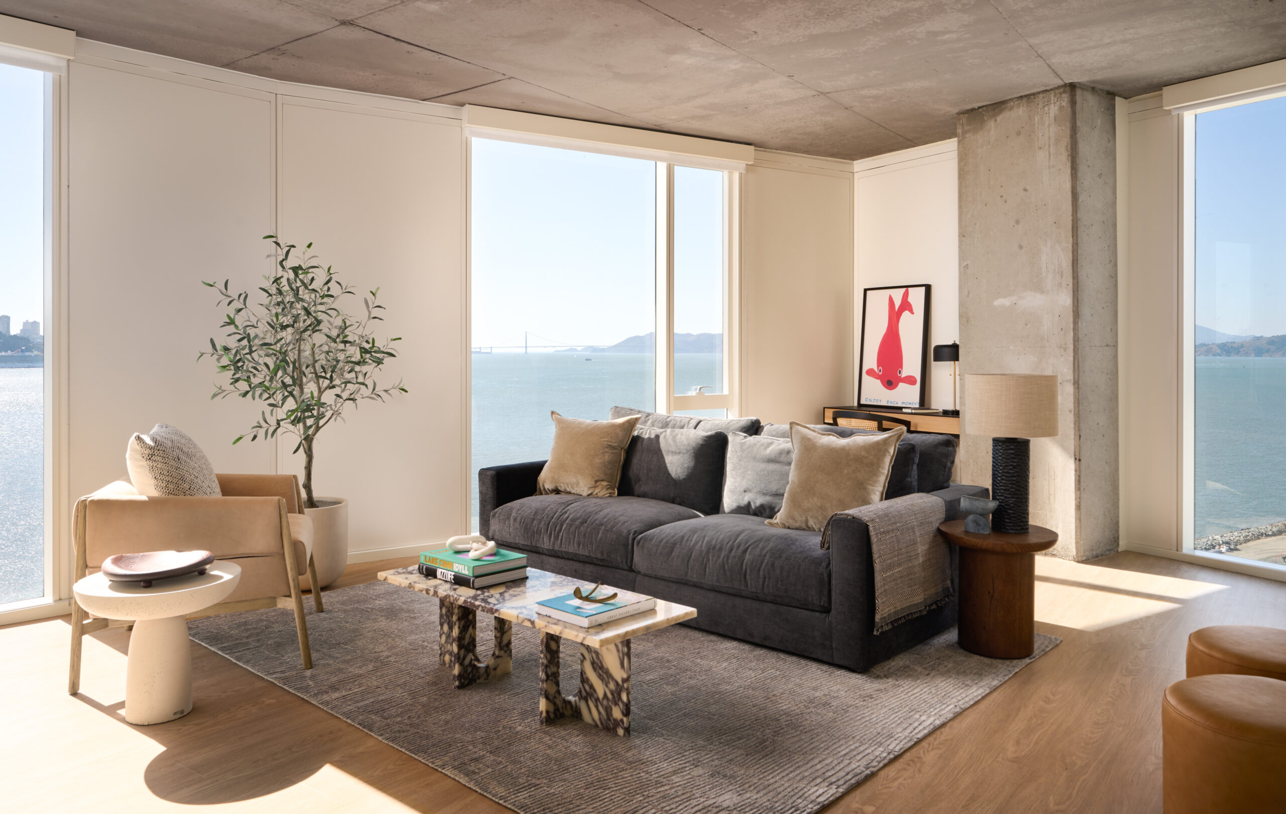 Sunlit waterfront living room at Isle House on Treasure Island with floor-to-ceiling windows overlooking the San Francisco Bay and Bay Bridge.