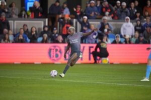 Professional soccer player kicking the ball during a Bay FC match with fans in the stadium stands behind her.