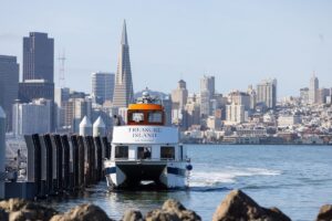 Treasure Island ferry arriving at the dock with the San Francisco skyline and Transamerica Pyramid in the background.