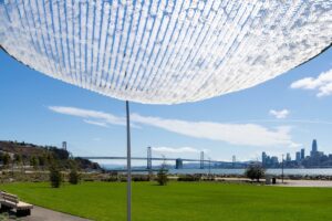 Canopy of the Sky art installation shading a waterfront lawn on Treasure Island with views of the Bay Bridge and San Francisco skyline.