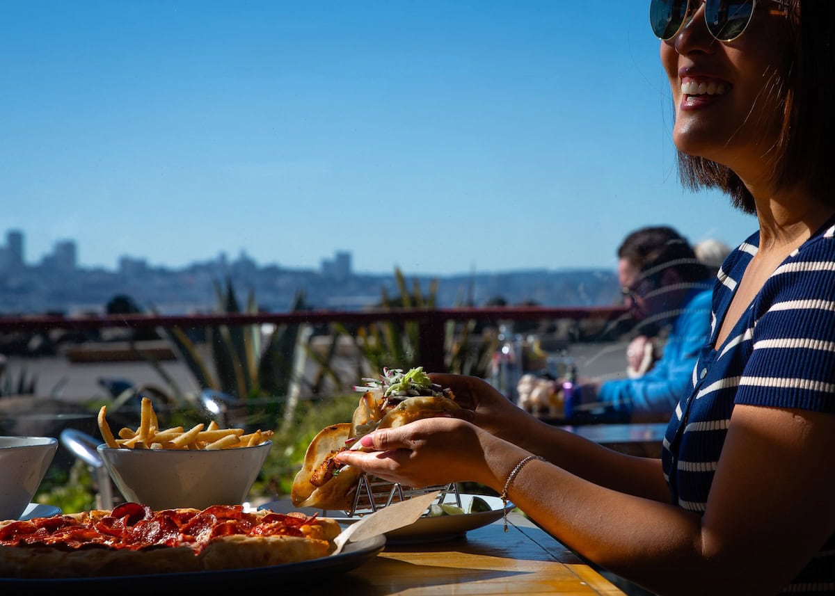 Woman eating pizza on outdoor patio overlooking San Francisco