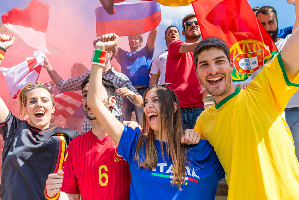 Cheering soccer fans in team jerseys waving international flags, representing World Cup watch party energy on Treasure Island.